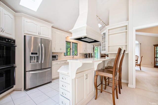 kitchen featuring white cabinetry, custom exhaust hood, stainless steel fridge with ice dispenser, a skylight, and double oven