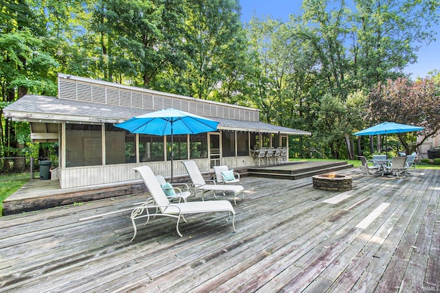 wooden deck with a sunroom and an outdoor fire pit