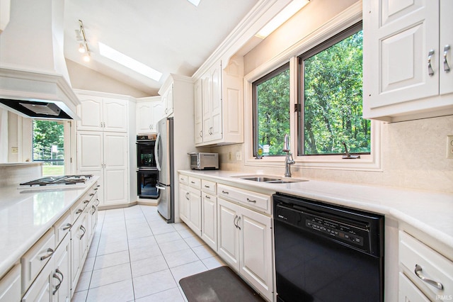 kitchen with lofted ceiling with skylight, dishwasher, white cabinets, light tile patterned floors, and gas cooktop