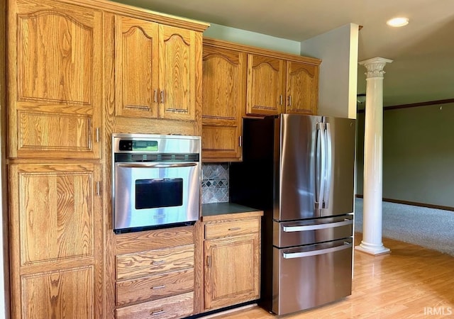 kitchen with decorative backsplash, stainless steel appliances, light hardwood / wood-style flooring, and ornate columns