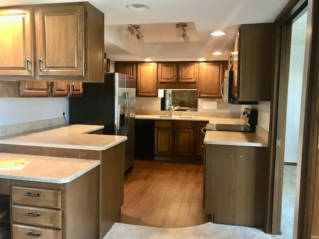 kitchen with sink, light wood-type flooring, a tray ceiling, kitchen peninsula, and stainless steel appliances