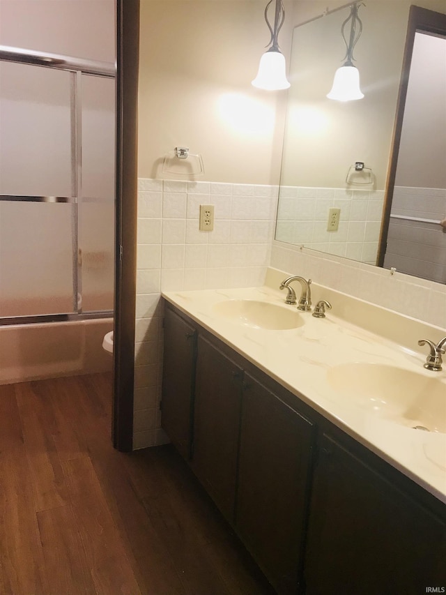 full bathroom with toilet, wood-type flooring, bath / shower combo with glass door, tile walls, and vanity