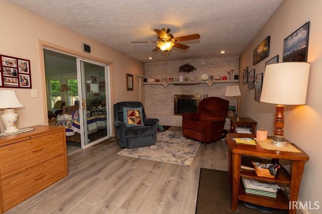 living room with a fireplace, ceiling fan, brick wall, light hardwood / wood-style flooring, and a textured ceiling