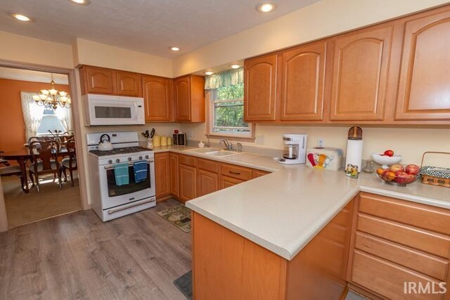 kitchen with white appliances, a chandelier, kitchen peninsula, carpet floors, and sink