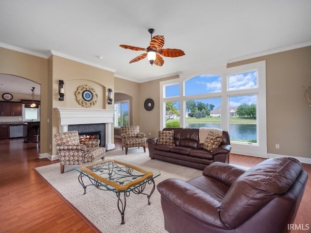 living room with a fireplace, wood-type flooring, ceiling fan, a water view, and crown molding