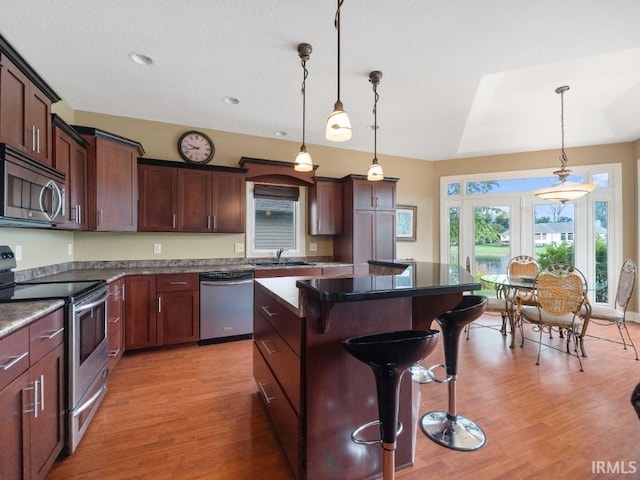 kitchen featuring stainless steel appliances, a breakfast bar, sink, hanging light fixtures, and light hardwood / wood-style floors