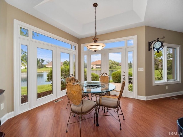 dining area with a tray ceiling, a water view, french doors, and hardwood / wood-style flooring