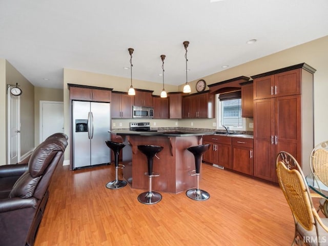 kitchen with a breakfast bar area, appliances with stainless steel finishes, decorative light fixtures, a kitchen island, and light wood-type flooring