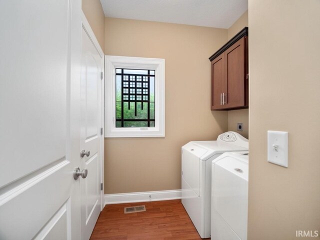 clothes washing area featuring washer and dryer, hardwood / wood-style floors, and cabinets