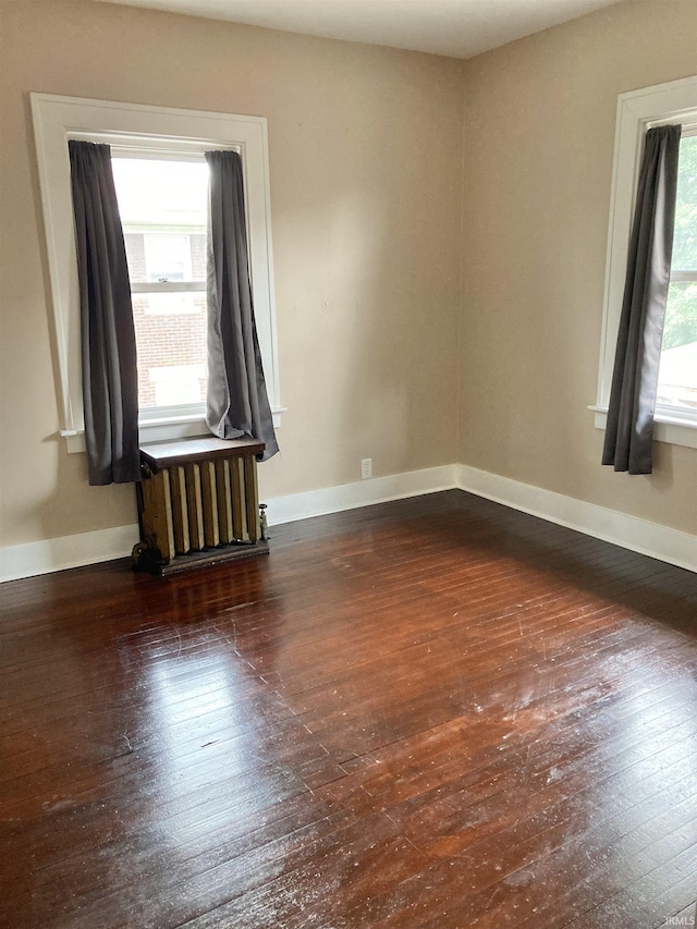 empty room with dark wood-type flooring and radiator heating unit