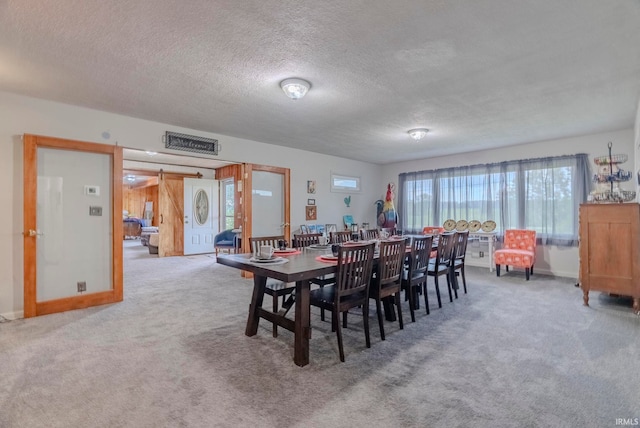 dining space with carpet floors, a barn door, and a textured ceiling