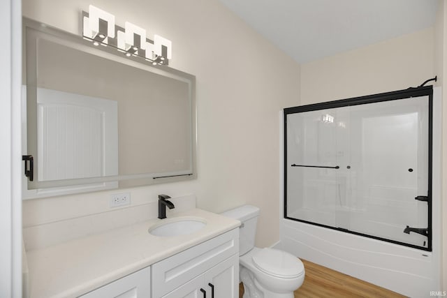 full bathroom with bath / shower combo with glass door, hardwood / wood-style floors, vanity, and toilet