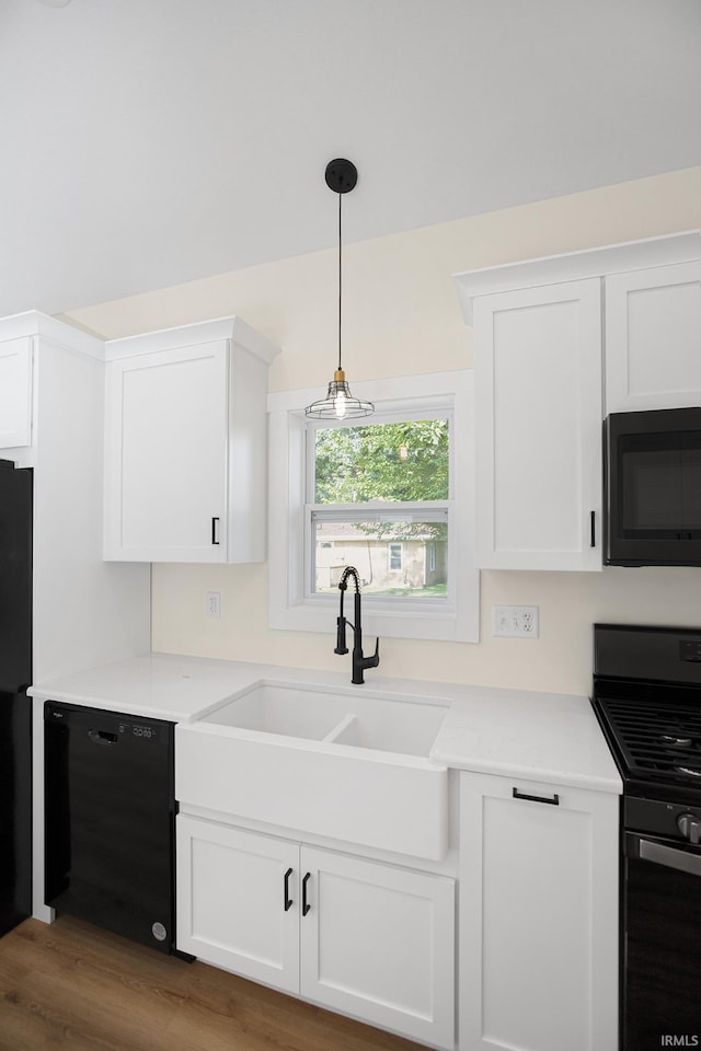 kitchen featuring black appliances, white cabinets, sink, decorative light fixtures, and wood-type flooring