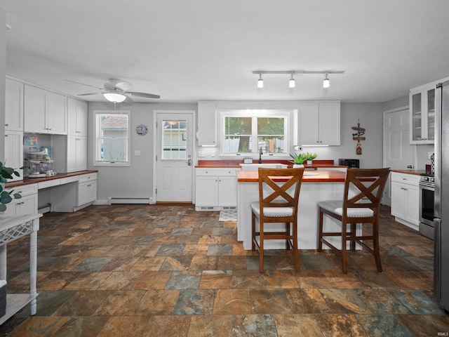 kitchen featuring ceiling fan, a baseboard radiator, a kitchen breakfast bar, and white cabinets