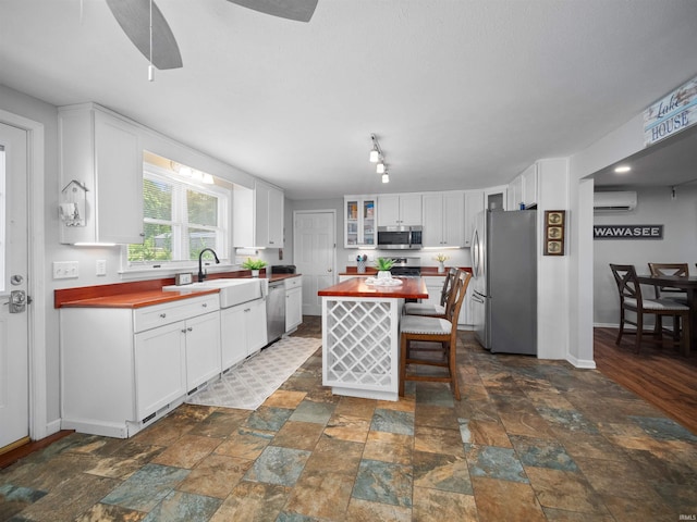 kitchen with wood counters, a wall mounted AC, stainless steel appliances, a kitchen island, and white cabinets