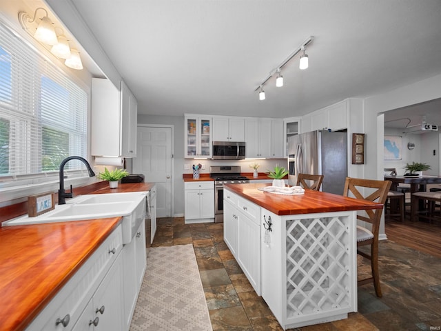 kitchen with stainless steel appliances, white cabinetry, wooden counters, and a center island