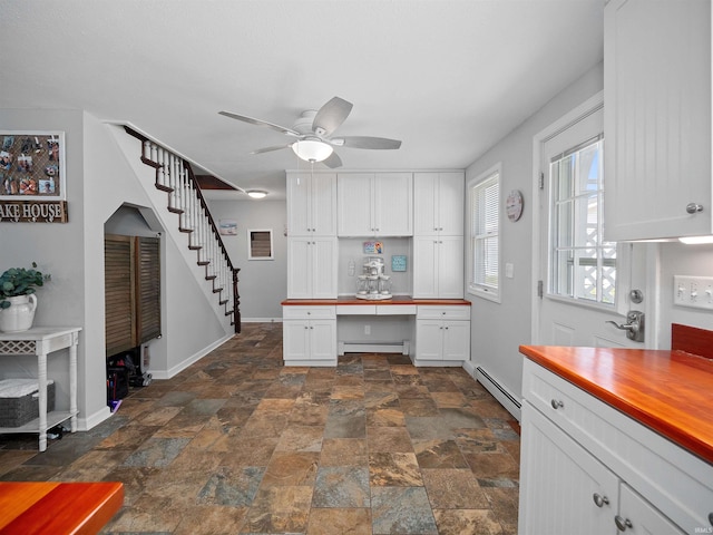 kitchen featuring a baseboard heating unit, ceiling fan, white cabinetry, and built in desk