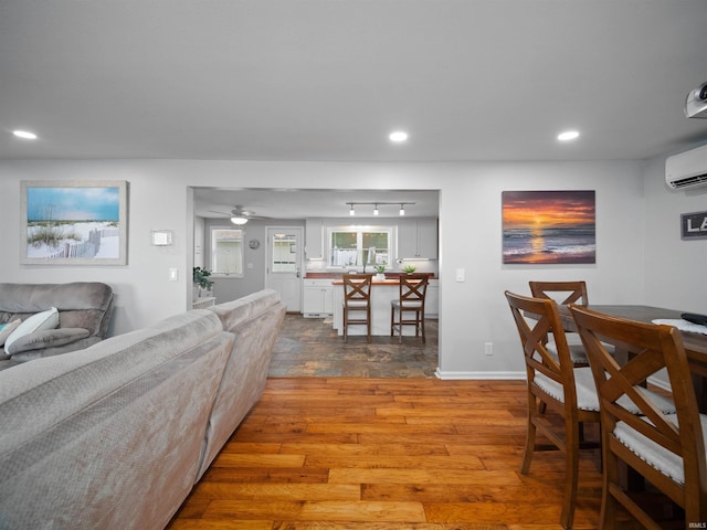 living room featuring an AC wall unit, wood-type flooring, and ceiling fan