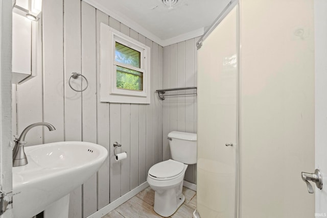 half bath featuring a sink, wood walls, toilet, and wood finished floors