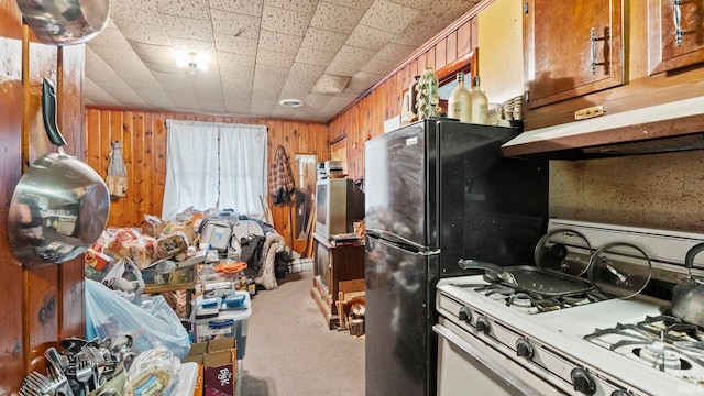 kitchen with carpet, white gas range oven, brown cabinetry, and freestanding refrigerator