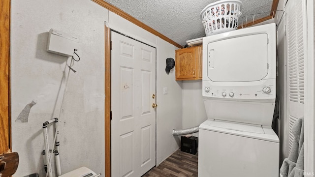 laundry area featuring stacked washer / dryer, a textured ceiling, dark hardwood / wood-style flooring, cabinets, and ornamental molding