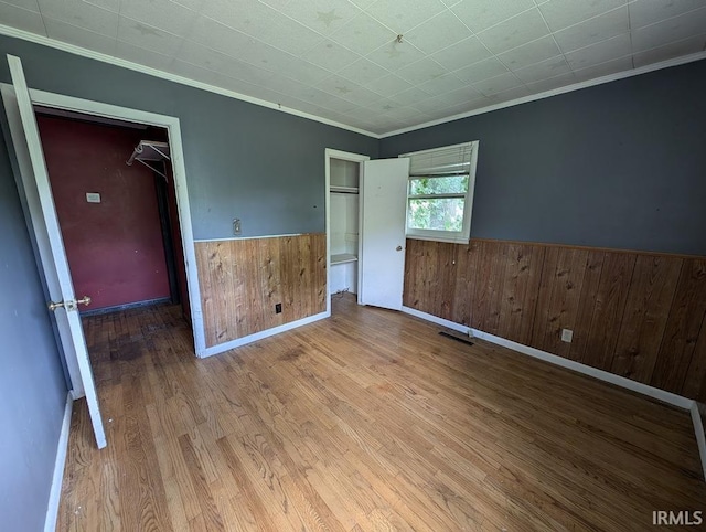 unfurnished bedroom featuring a wainscoted wall, visible vents, ornamental molding, wooden walls, and wood finished floors