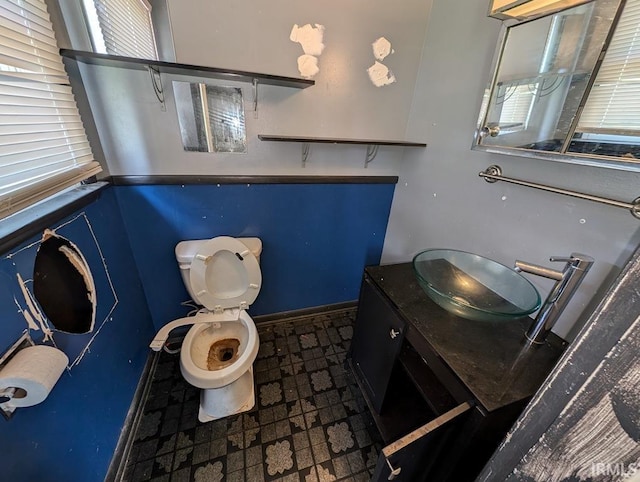 half bath with baseboards, vanity, and toilet