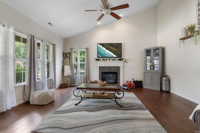 living room featuring ceiling fan, dark hardwood / wood-style floors, a tile fireplace, and plenty of natural light