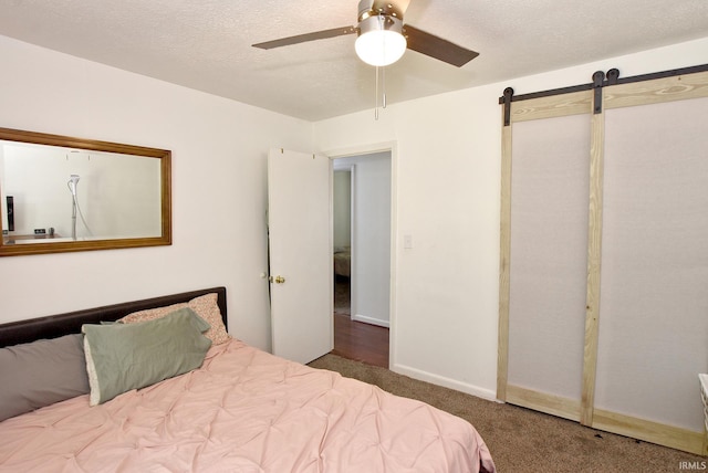 bedroom featuring a textured ceiling, ceiling fan, carpet, and a barn door