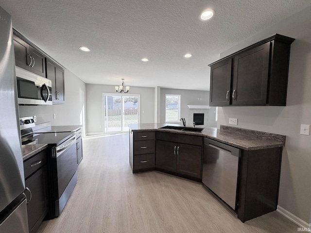 kitchen with appliances with stainless steel finishes, decorative light fixtures, sink, dark brown cabinets, and light hardwood / wood-style flooring