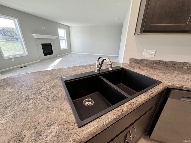 kitchen featuring sink, light colored carpet, a fireplace, and dark brown cabinetry