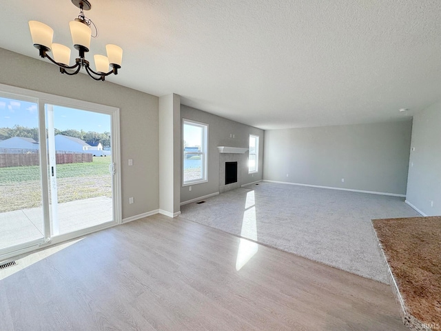 unfurnished living room with a chandelier, light hardwood / wood-style flooring, and a textured ceiling