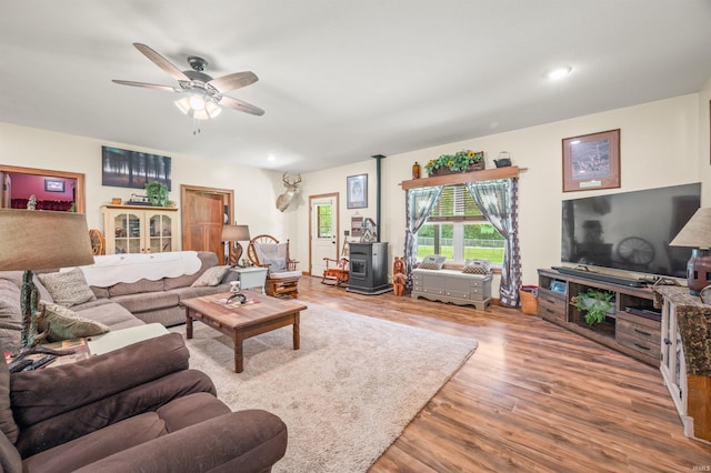 living room featuring a wood stove, wood-type flooring, and ceiling fan