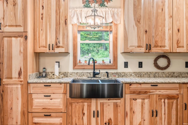 kitchen with light brown cabinetry, sink, a chandelier, and light stone counters