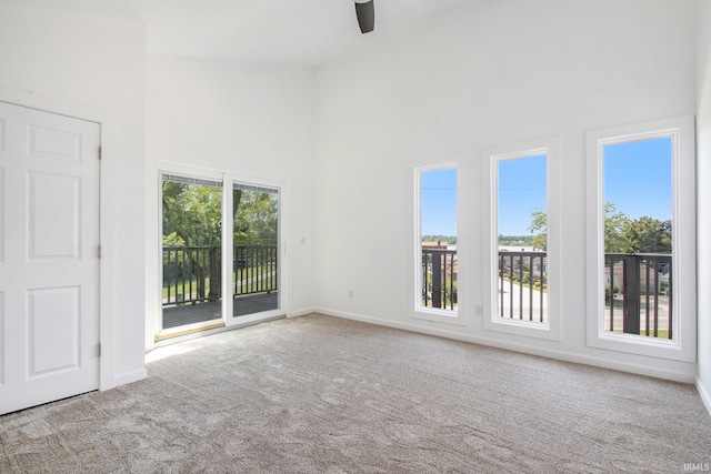 unfurnished room with light carpet, ceiling fan, and a towering ceiling