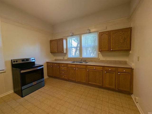 kitchen featuring stainless steel electric stove, light floors, light countertops, a sink, and brown cabinets
