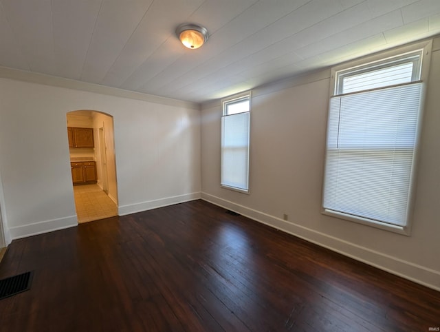 unfurnished room with visible vents, baseboards, arched walkways, and dark wood finished floors