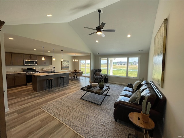 living room featuring wood-type flooring, sink, ceiling fan with notable chandelier, and high vaulted ceiling