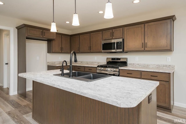 kitchen featuring sink, decorative light fixtures, a center island with sink, light wood-type flooring, and stainless steel appliances