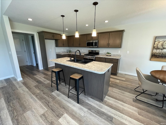 kitchen featuring appliances with stainless steel finishes, decorative light fixtures, an island with sink, sink, and light hardwood / wood-style floors