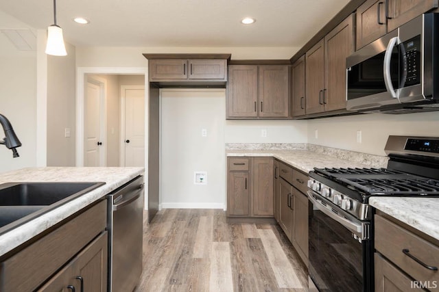 kitchen with sink, hanging light fixtures, stainless steel appliances, light stone counters, and light hardwood / wood-style floors