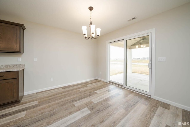 unfurnished dining area with an inviting chandelier and light wood-type flooring