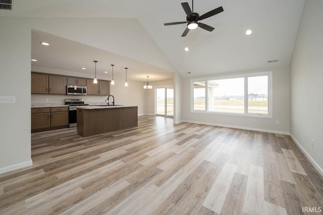 kitchen featuring light hardwood / wood-style flooring, appliances with stainless steel finishes, high vaulted ceiling, an island with sink, and decorative light fixtures