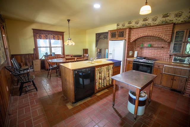 kitchen with gas range, white refrigerator with ice dispenser, black dishwasher, pendant lighting, and a center island with sink