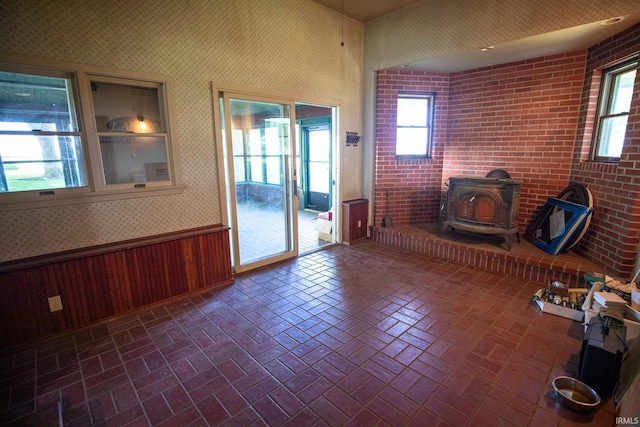 unfurnished room featuring a wood stove, brick wall, and a wealth of natural light