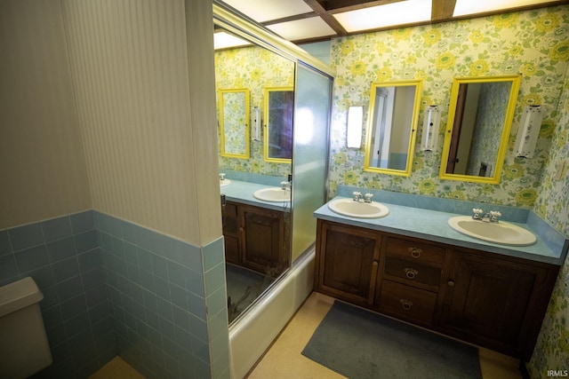 full bathroom featuring toilet, combined bath / shower with glass door, double sink vanity, and tile walls