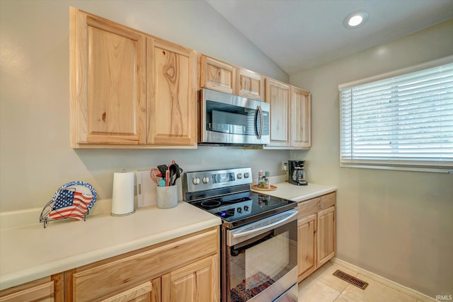 kitchen featuring vaulted ceiling, stainless steel appliances, light brown cabinetry, and light tile patterned flooring