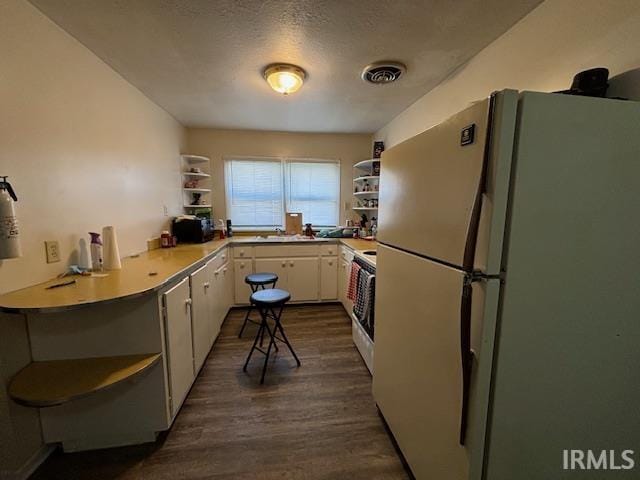 kitchen featuring white cabinets, white appliances, kitchen peninsula, dark wood-type flooring, and a textured ceiling