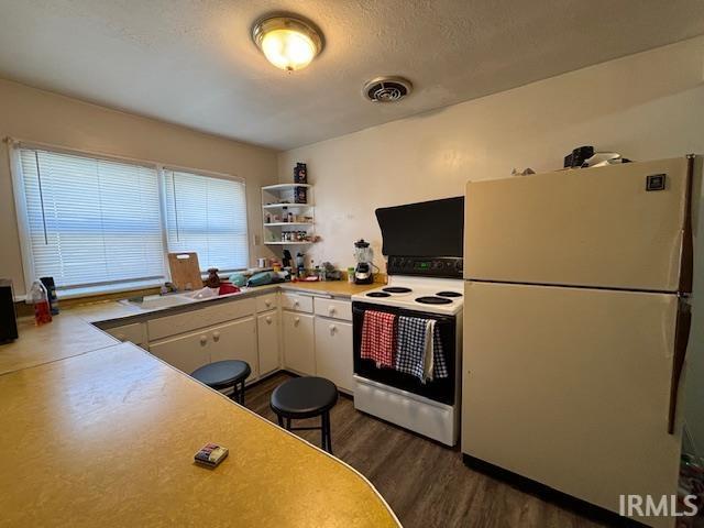 kitchen featuring white cabinetry, a textured ceiling, dark hardwood / wood-style flooring, kitchen peninsula, and white appliances