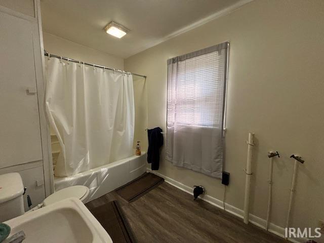 bathroom with wood-type flooring, shower / bath combination with curtain, and toilet